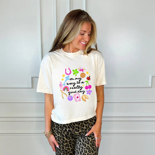 Woman wearing a white t-shirt with colorful graphics and text, standing against a white wall.