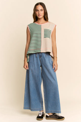Woman wearing a colorful sleeveless top and blue jeans on a beige background