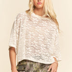 Woman wearing a white lace top and patterned pants against a beige background