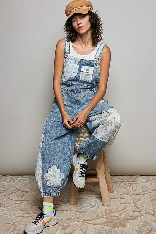 Denim coveralls with patches and a white tank top on model with hat on stool