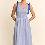 Woman wearing a blue and white striped dress with suspenders on a beige background