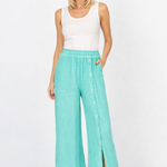 Woman wearing a white sleeveless top and teal wide-leg pants on a white background