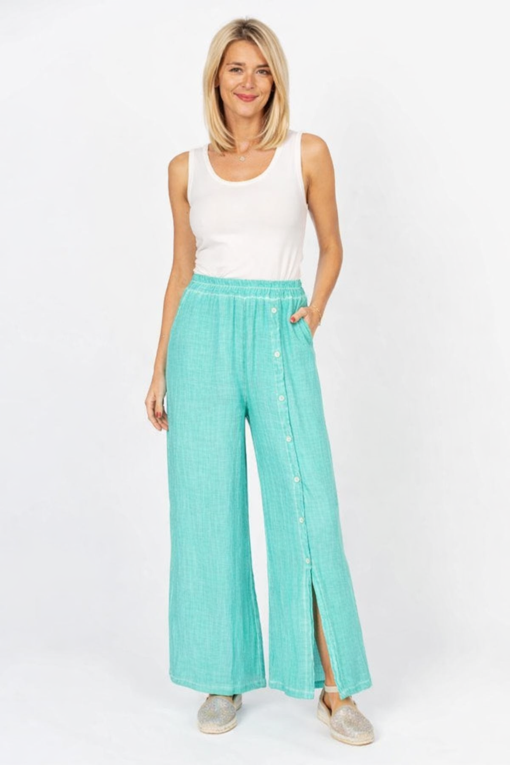 Woman wearing a white sleeveless top and teal wide-leg pants on a white background