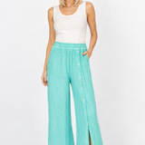 Woman wearing a white sleeveless top and teal wide-leg pants on a white background