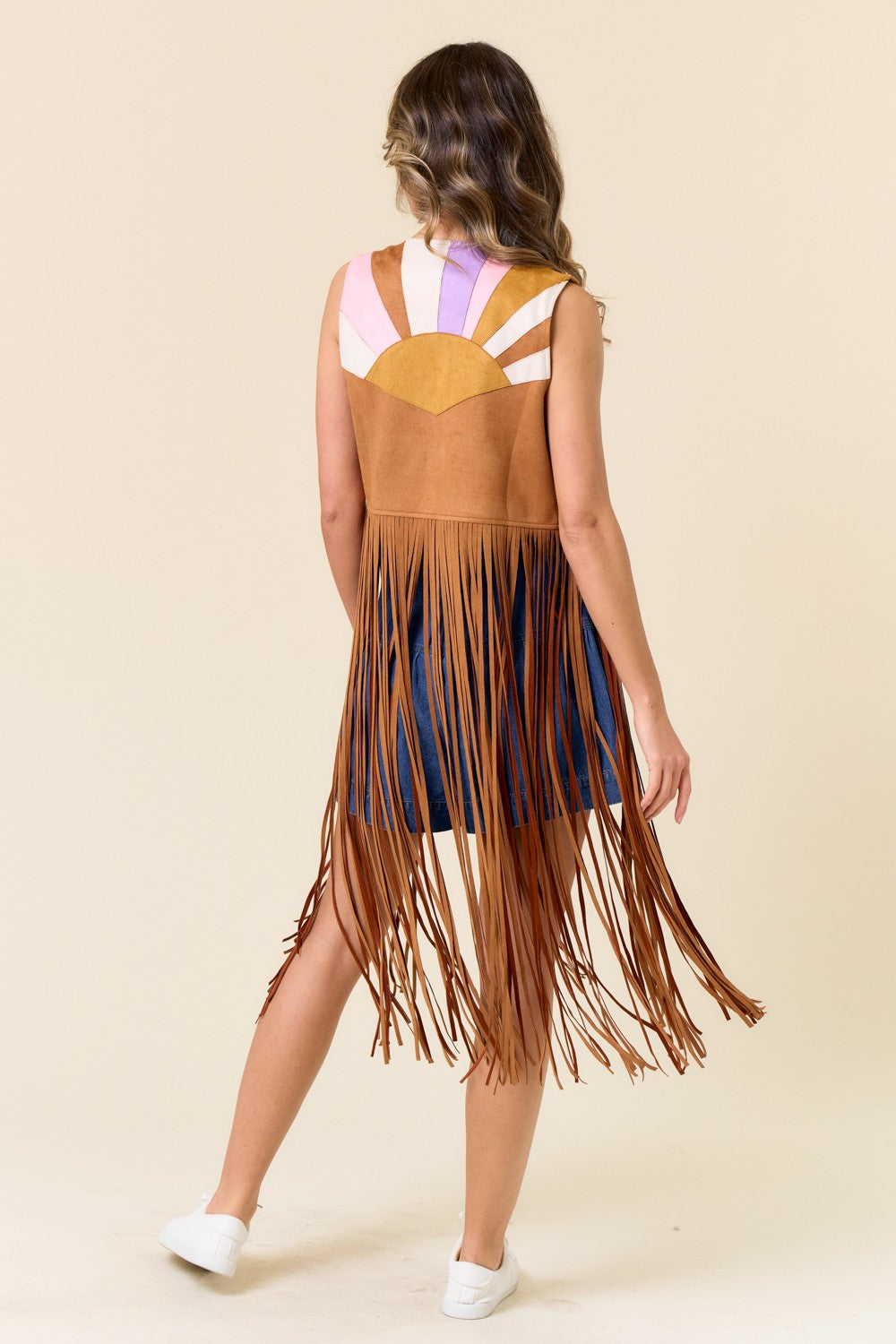 Woman wearing a fringed dress with a colorful top on a beige background