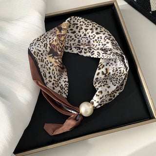 Leopard print scarf with a pearl and brown ribbon in a black box on a white surface