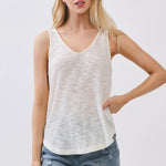 Woman wearing a white sleeveless top and denim shorts on a plain background