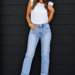 Woman wearing a white top and light blue jeans against a black wooden panel background