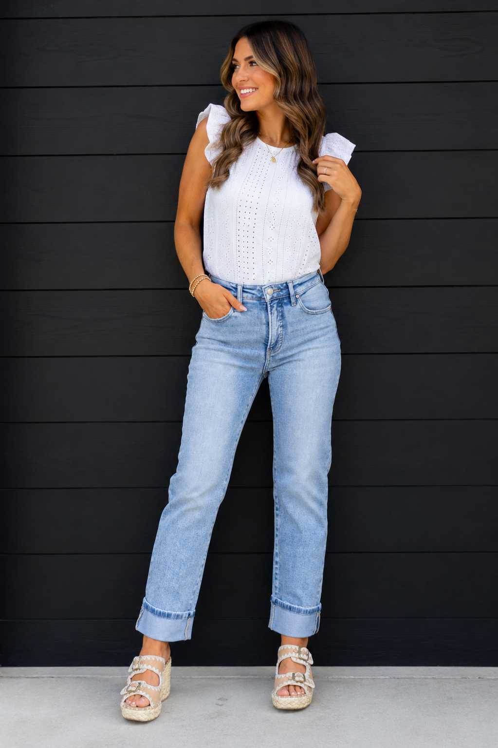 Woman wearing a white top and light blue jeans against a black wooden panel background