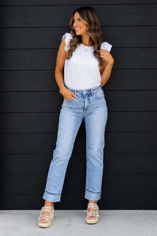 Woman wearing a white top and light blue jeans against a black wooden panel background