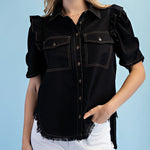Woman wearing a black denim shirt with ruffled sleeves against a light blue background