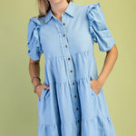 Woman wearing a light blue dress with ruffled sleeves against a green background