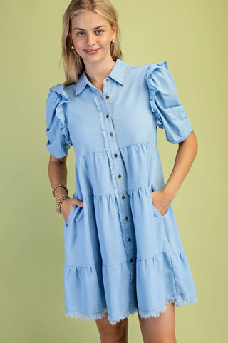 Woman wearing a light blue dress with ruffled sleeves against a green background