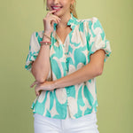 Woman wearing a patterned shirt and white shorts against a green background