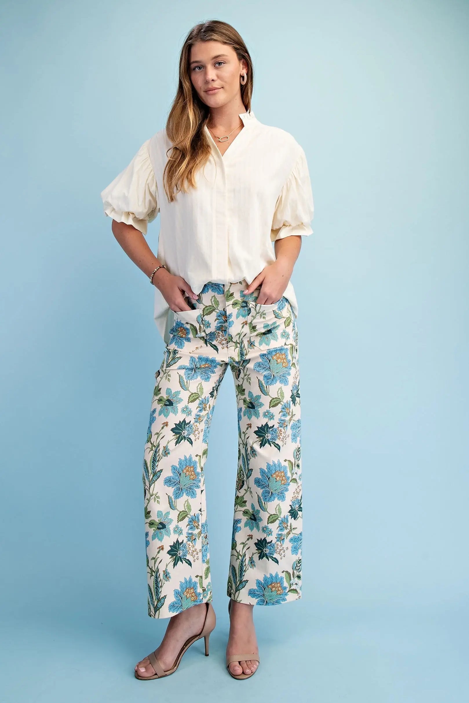 Woman wearing a white blouse and floral pants against a light blue background