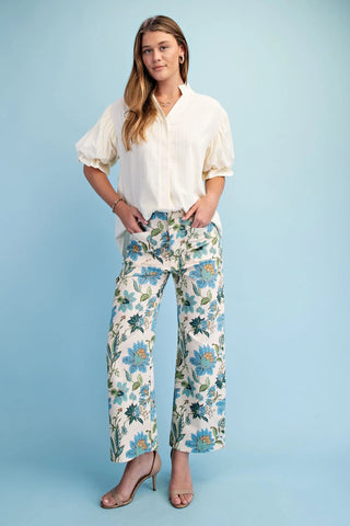 Woman wearing a white blouse and floral pants against a light blue background