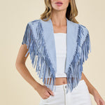 Woman wearing a light blue fringe jacket over a white top and pants on a beige background