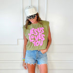Person wearing a sleeveless green shirt with 'Jesus Loves You' in pink text, denim shorts, and a white cap.