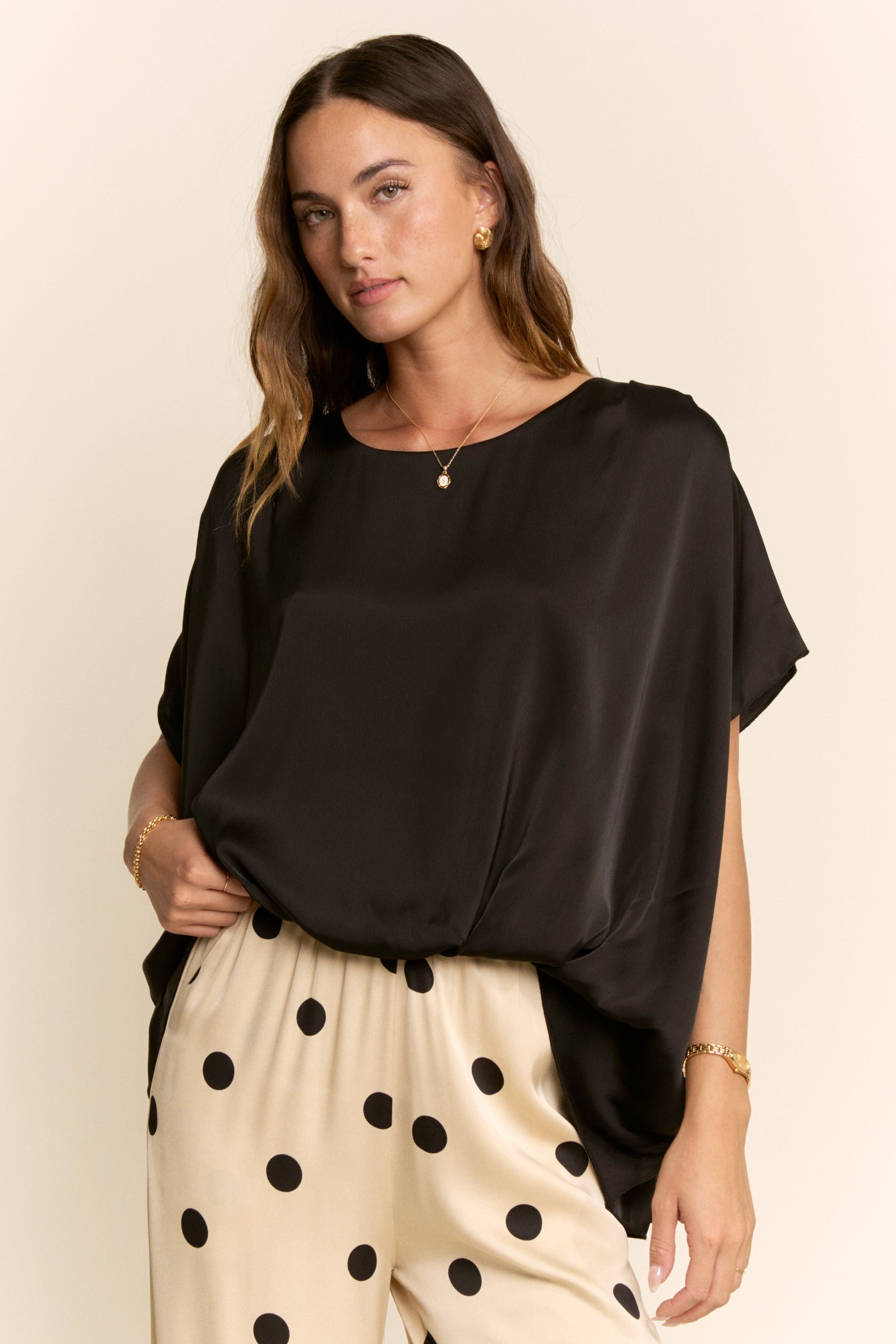 Woman wearing a black top and beige pants with black polka dots on a beige background