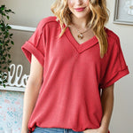Woman wearing a red ribbed top and blue jeans indoors.