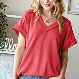 Woman wearing a red ribbed top and blue jeans indoors.