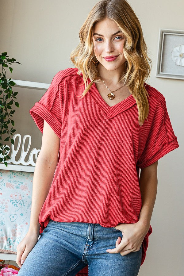 Woman wearing a red ribbed top and blue jeans indoors.