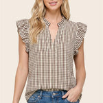 Woman wearing a checkered top with ruffled sleeves and blue jeans on a beige background