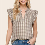 Woman wearing a checkered top with ruffled sleeves and blue jeans on a beige background