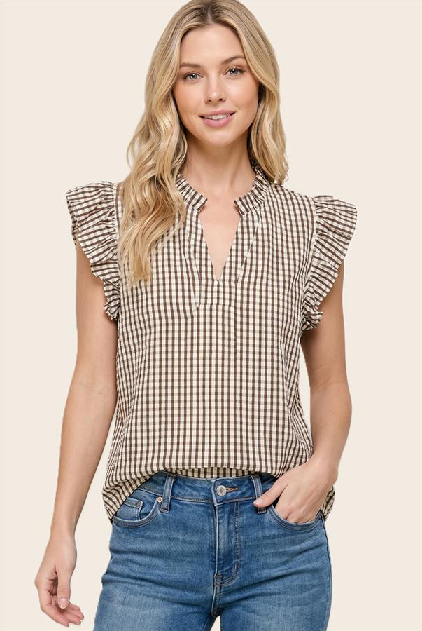 Woman wearing a checkered top with ruffled sleeves and blue jeans on a beige background