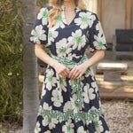 Woman wearing a navy floral dress standing outdoors near a tree.