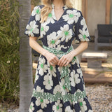 Woman wearing a navy floral dress standing outdoors near a tree.