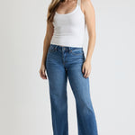 Woman wearing a white tank top and blue jeans on a plain background