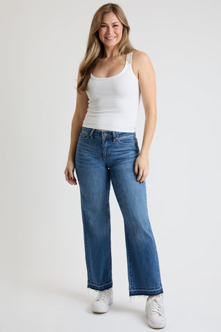 Woman wearing a white tank top and blue jeans on a plain background