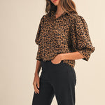 Woman wearing a leopard print blouse and black pants on a beige background