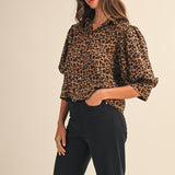 Woman wearing a leopard print blouse and black pants on a beige background