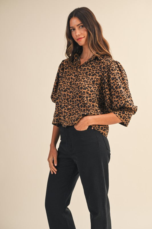 Woman wearing a leopard print blouse and black pants on a beige background