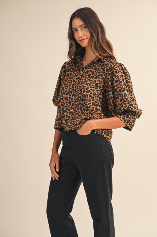 Woman wearing a leopard print blouse and black pants on a beige background