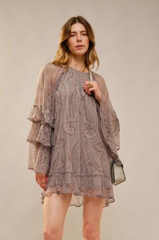 Woman wearing a layered dress with sheer sleeves against a plain background