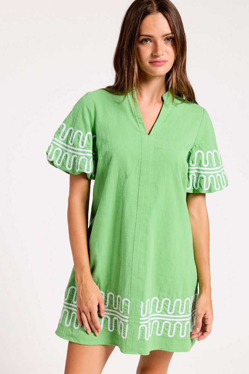 Woman wearing a green dress with white embroidery on a white background
