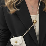Person wearing a black blazer with a white quilted handbag featuring gold accents.