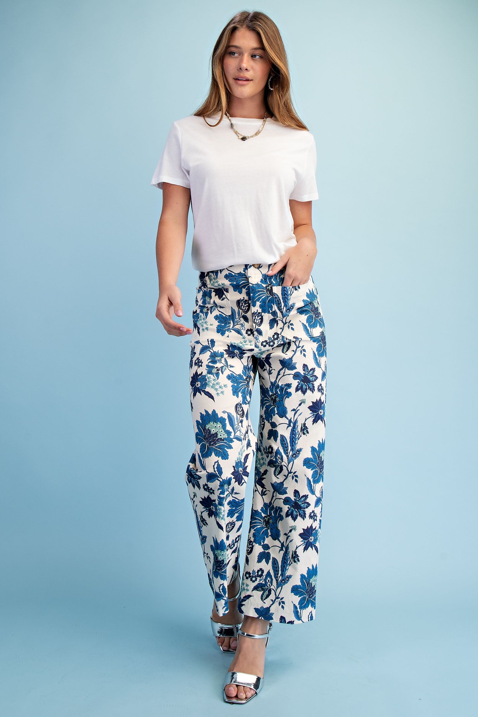 Woman wearing a white t-shirt and blue floral pants on a light blue background