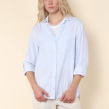 Woman wearing a light blue shirt and beige pants against a beige background