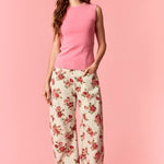 Woman wearing a pink sleeveless top and floral pants on a pink background