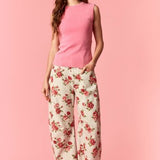 Woman wearing a pink sleeveless top and floral pants on a pink background