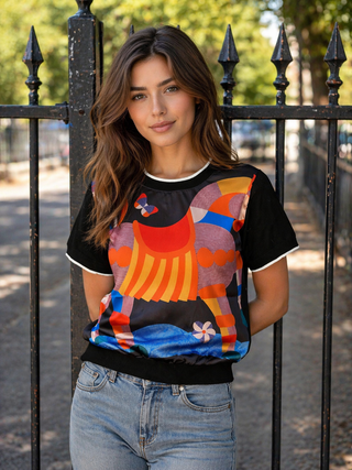 Woman wearing a colorful graphic t-shirt standing in front of a black metal fence.