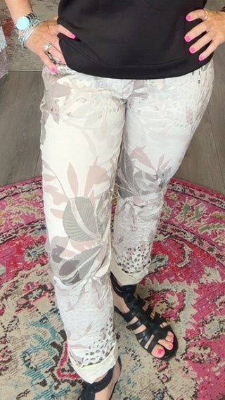 A woman stands in a boutique shop wearing a black short-sleeve top and light beige patterned pants, posing on a round patterned rug.