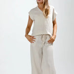 Woman wearing a beige sleeveless top and wide-leg pants on a white background