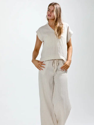 Woman wearing a beige sleeveless top and wide-leg pants on a white background