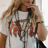 Woman wearing a white t-shirt with red and black lettering, layered necklaces, and leopard print pants.