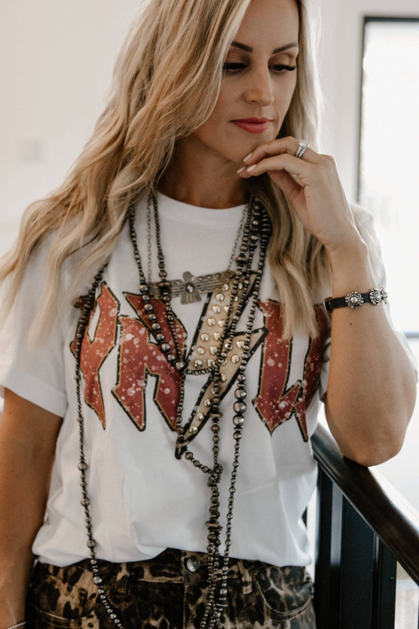 Woman wearing a white t-shirt with red and black lettering, layered necklaces, and leopard print pants.